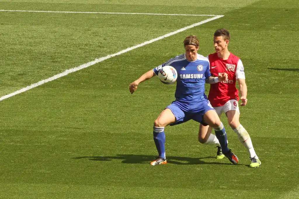 Fernando Torres w niebieskim stroju Chelsea opanowuje piłkę, a za nim stoi Laurent Koscielny.