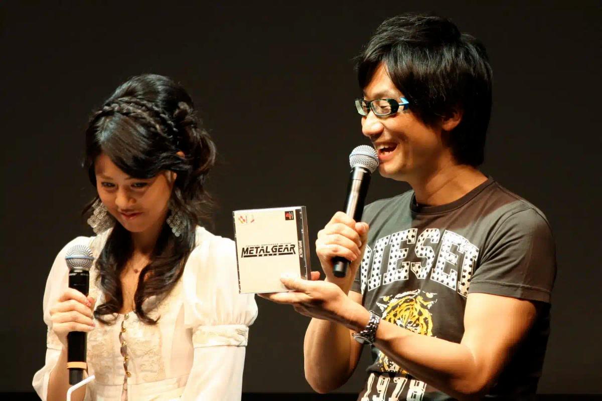 Hideo Kojima trzymający pudełko z grą Metal Gear i mówiący do mikrofonu.